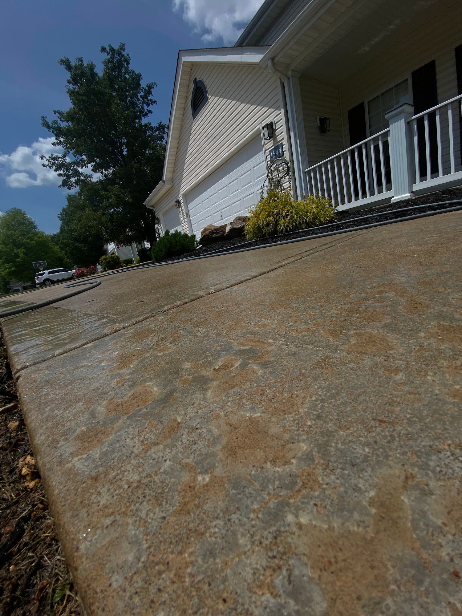 Concrete driveway leading up to a house with a white garage door and porch. Green shrubbery visible.
