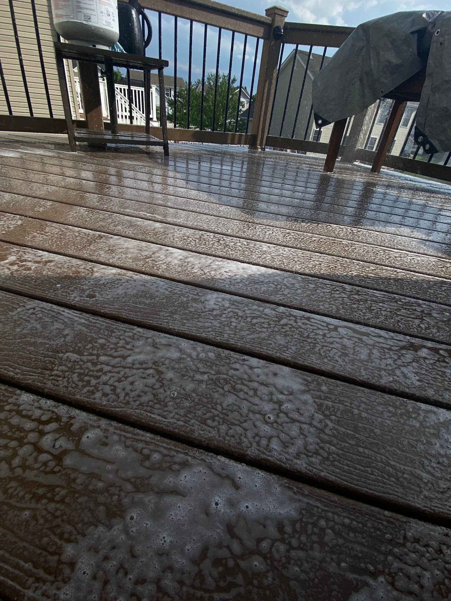 Deck with foamy cleaning solution applied, sunlight, outdoor setting.