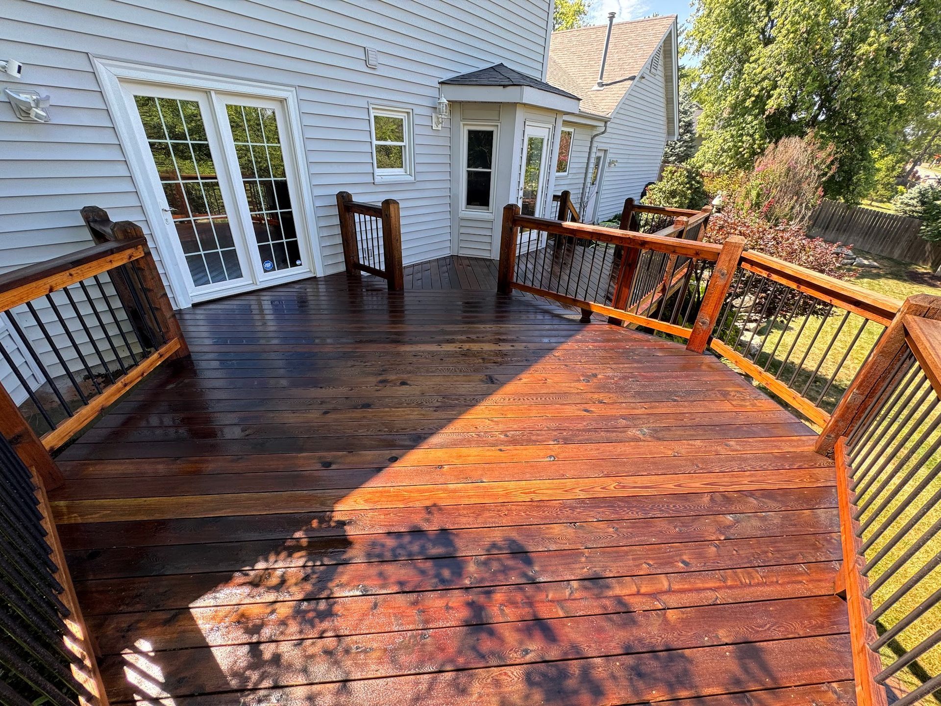 Wooden deck with dark stain, black railings, and glass doors leading to a light blue house.