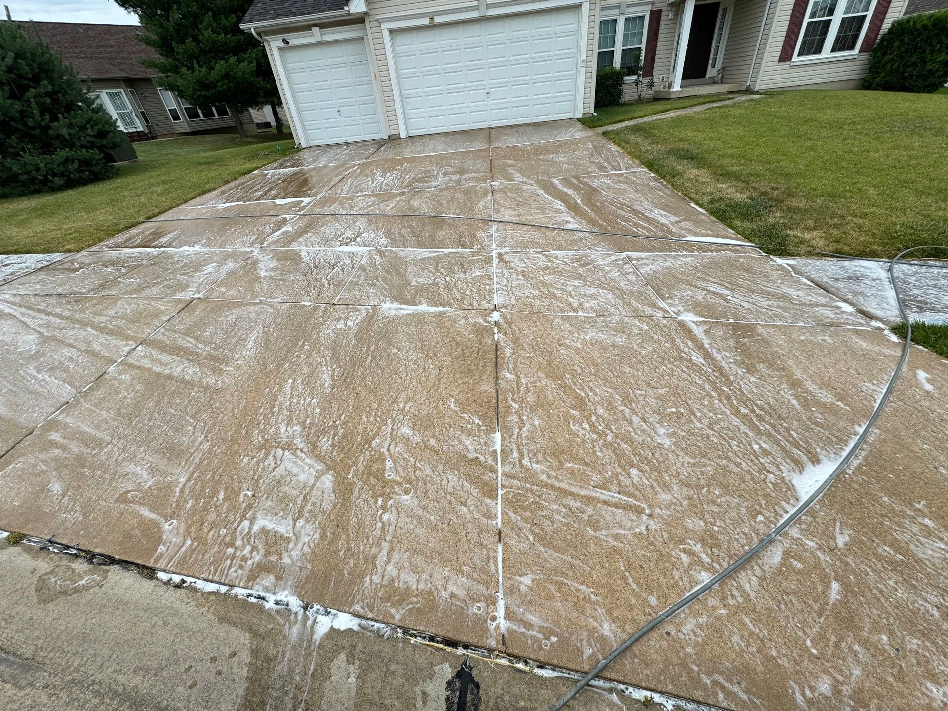 Driveway being cleaned with soap, near a house with a white garage door.