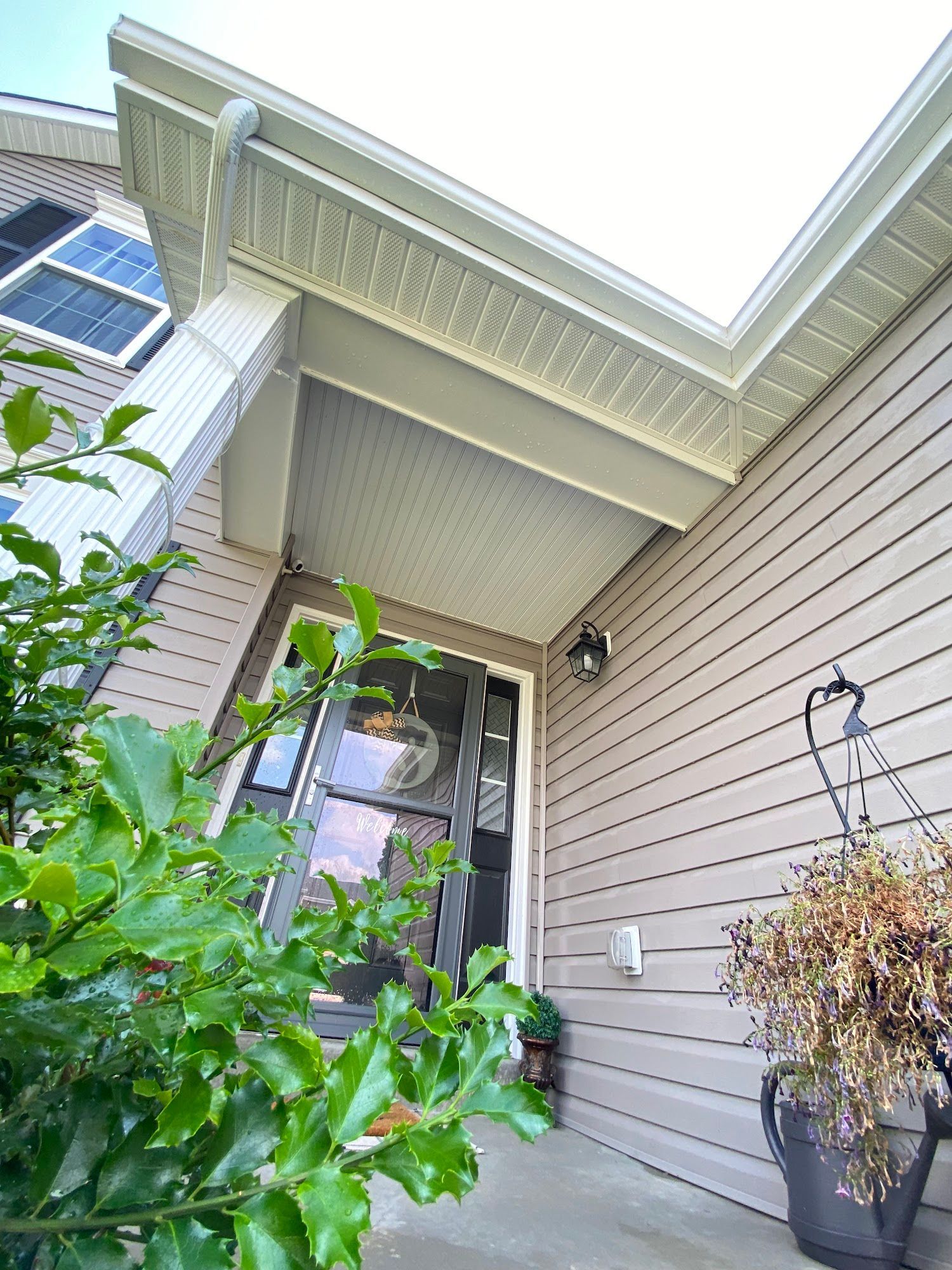 Entryway of a house with light brown siding, porch overhang, and a hanging basket with dried flowers.