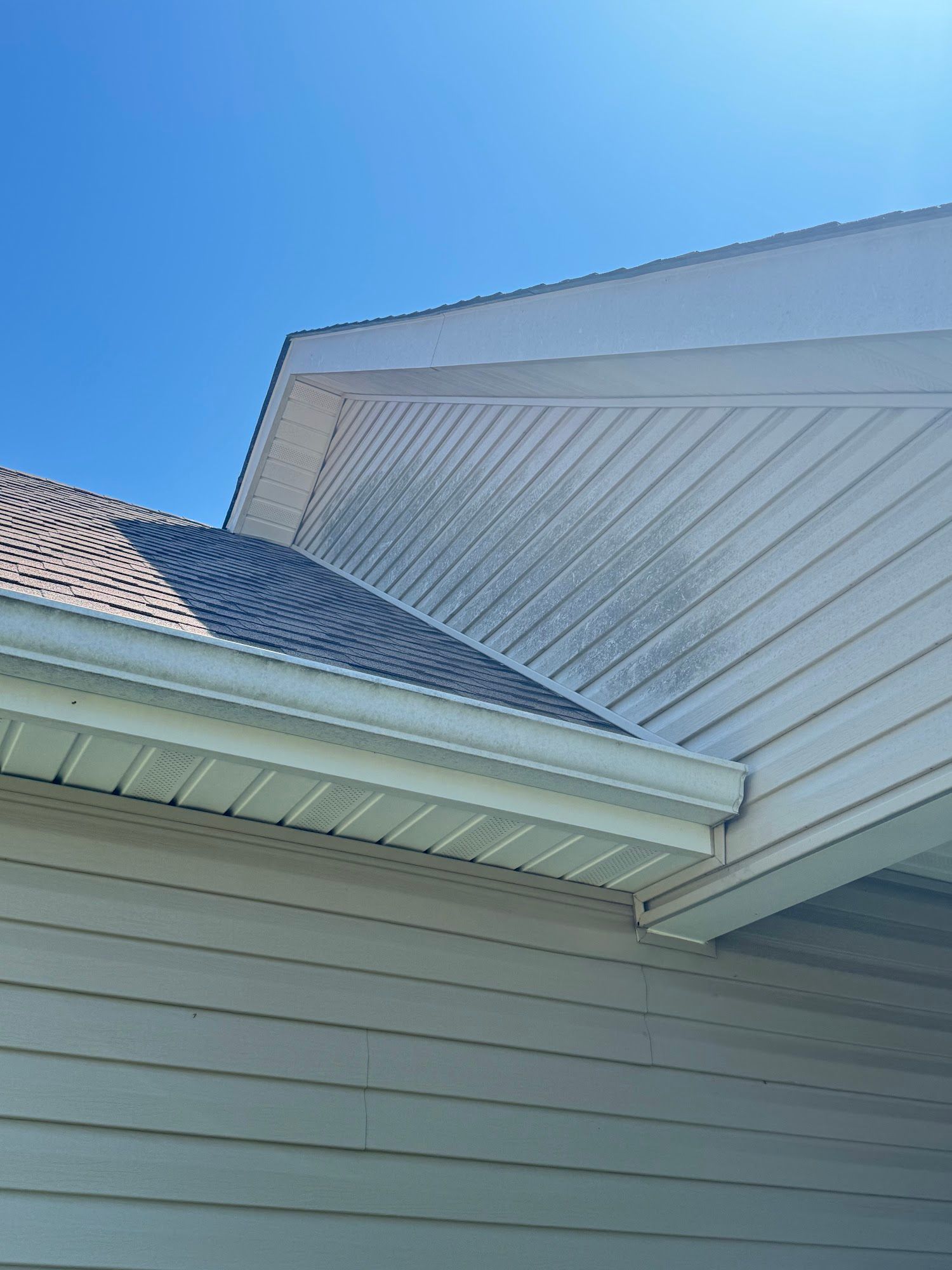 Corner of a house with a dirty white siding, roof, and blue sky background.