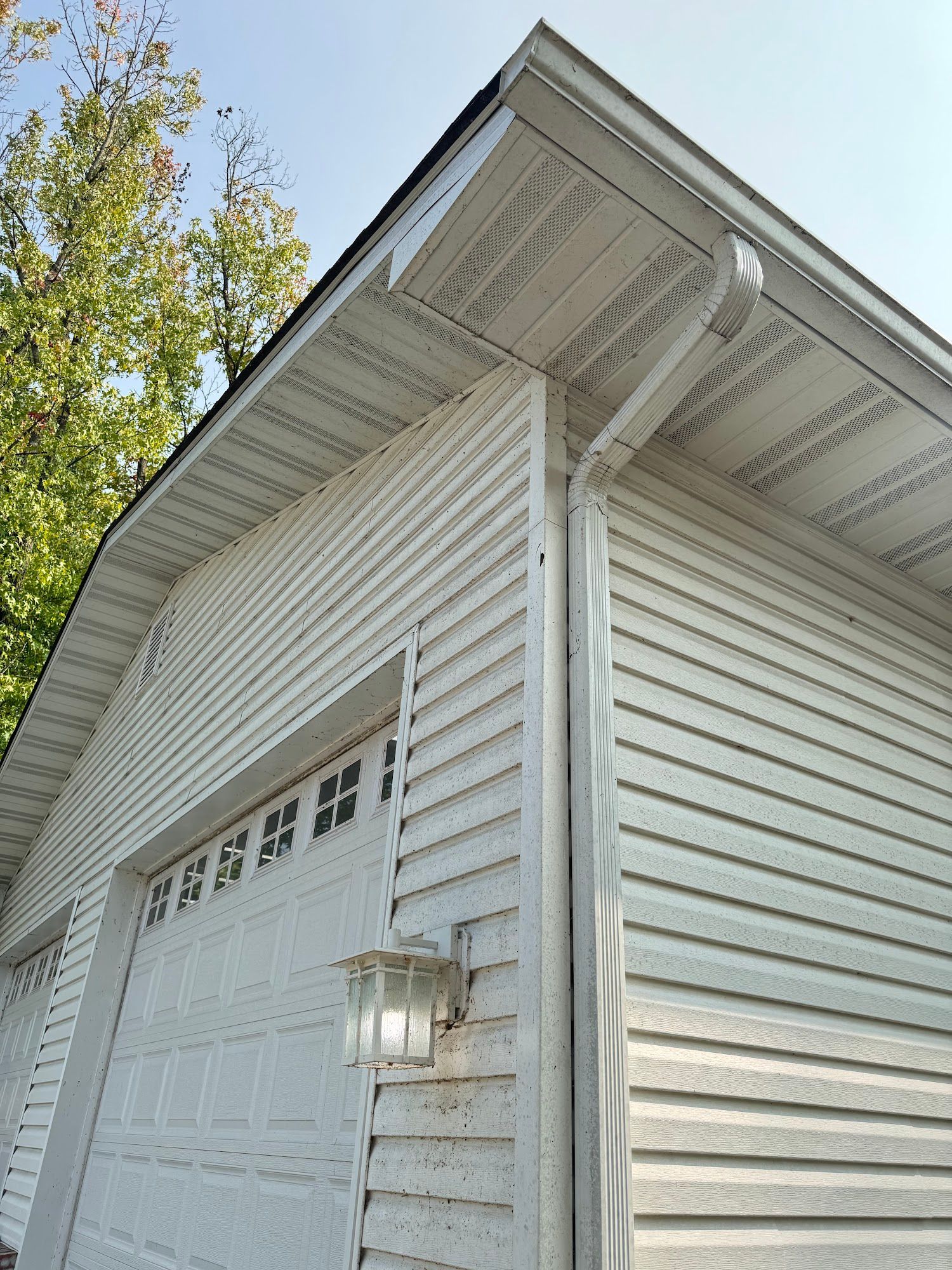 White vinyl-sided garage with a white garage door, gutters, and roof. A light fixture is mounted on the wall.