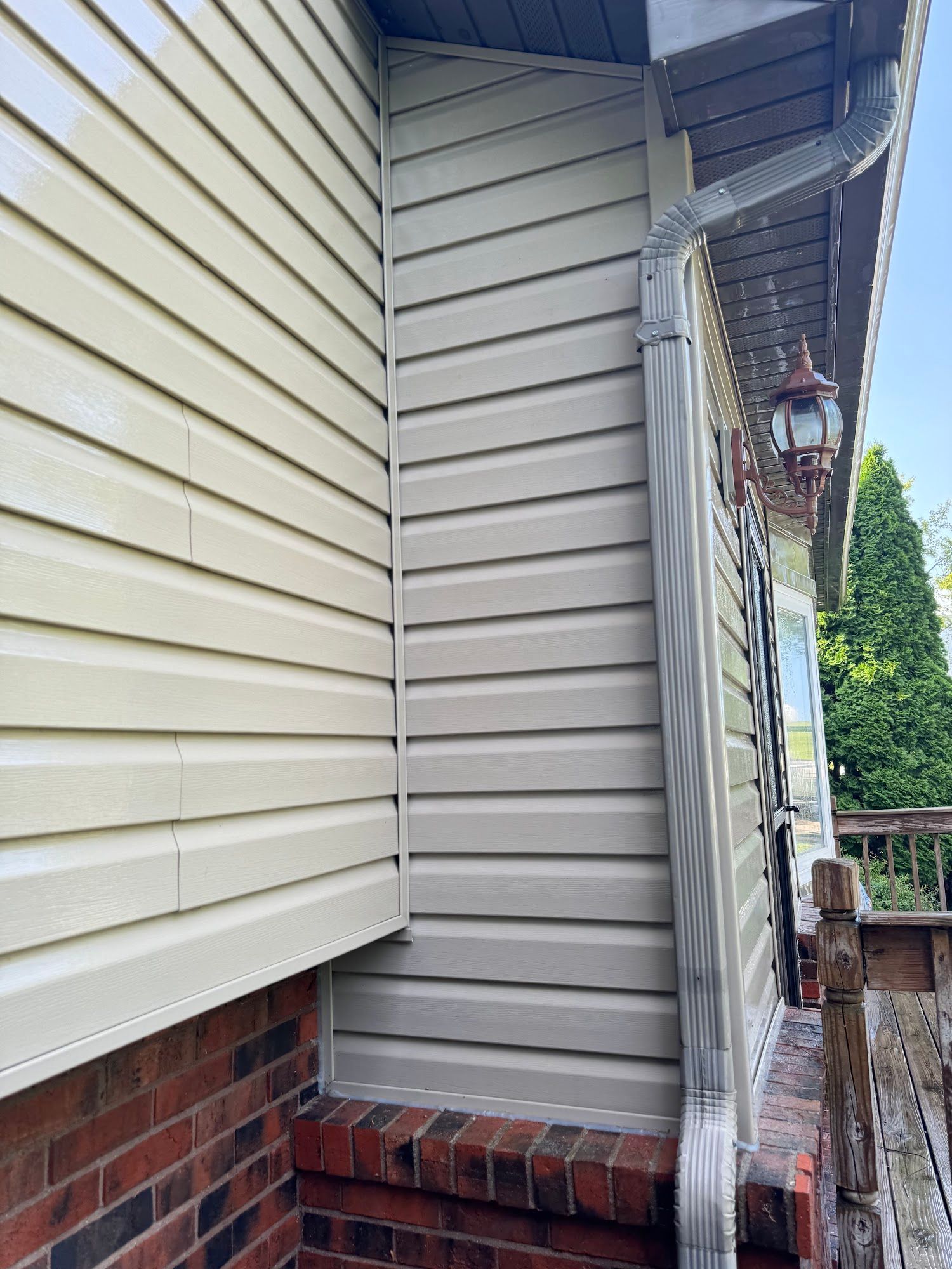 Tan vinyl siding on a house corner, with a gutter and brick foundation.