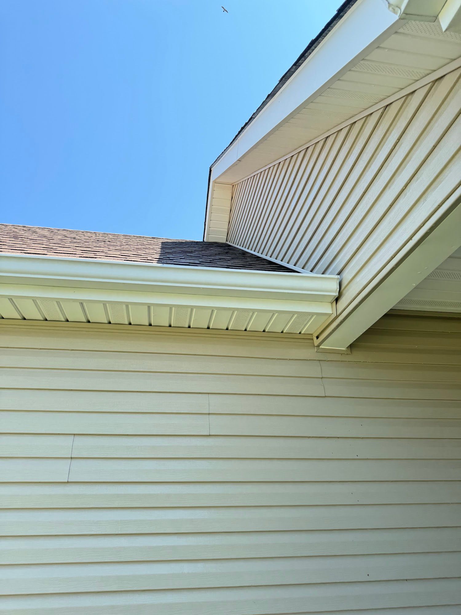 View of the corner of a house with light yellow siding, roof, and a blue sky.