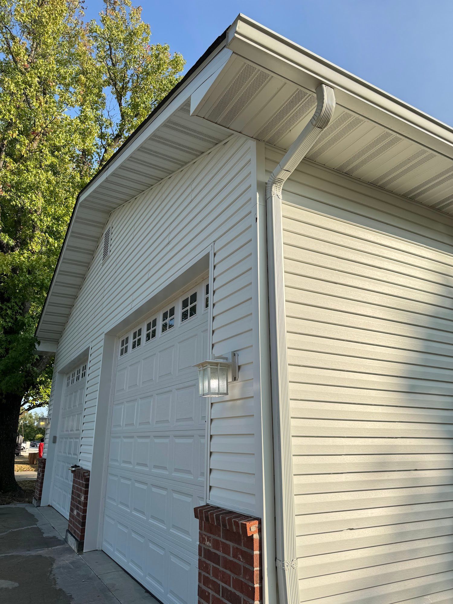 White garage with light siding and two garage doors, brick accents.