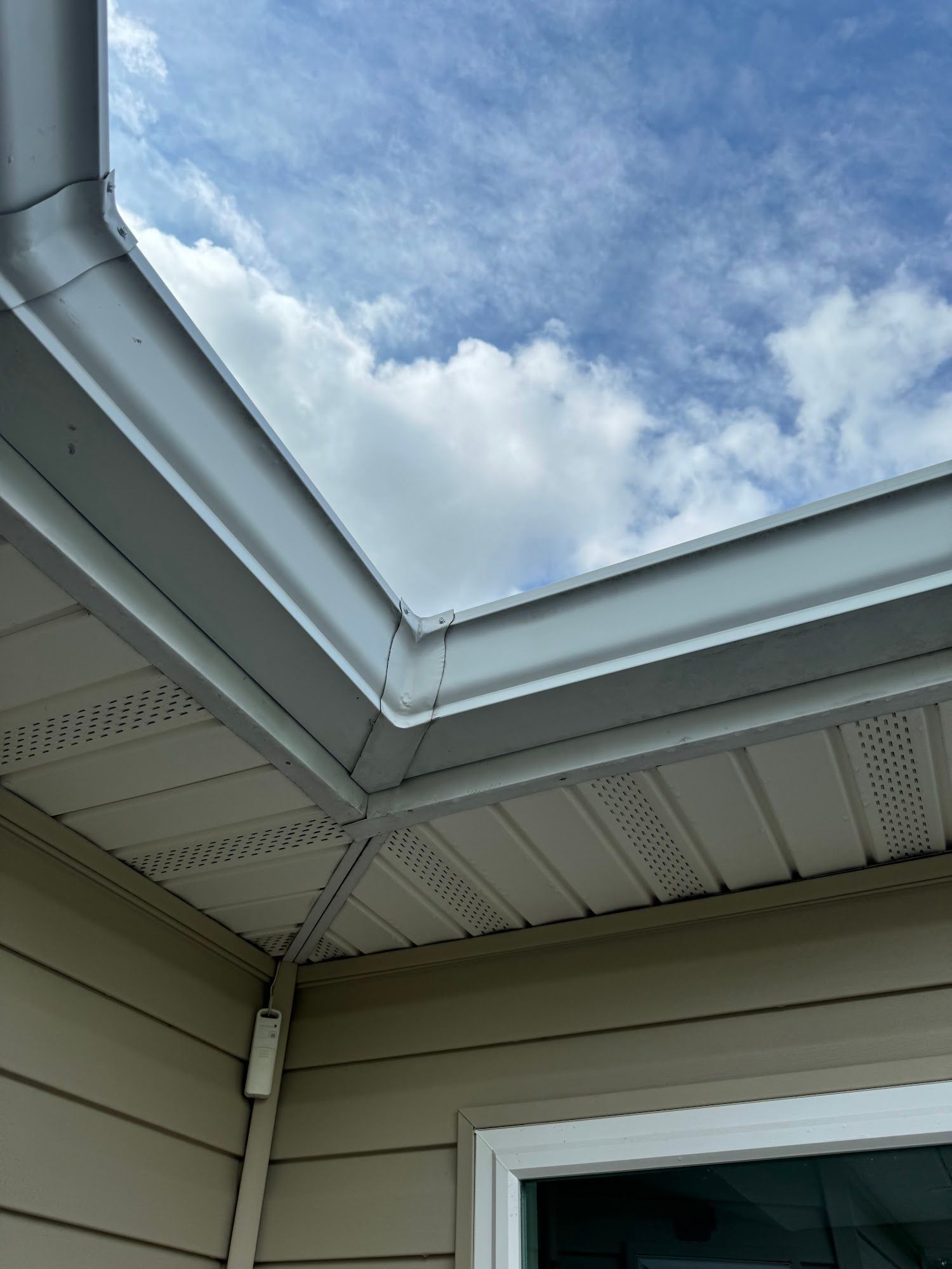 White gutters, soffit, and siding against a blue sky with fluffy clouds.