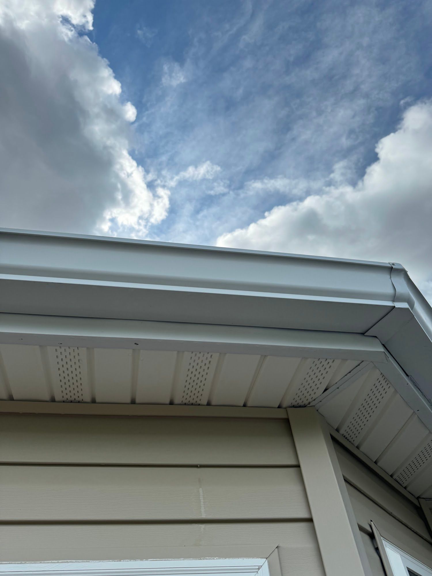 Exterior house detail, white trim and soffit, beige siding, blue sky with clouds.