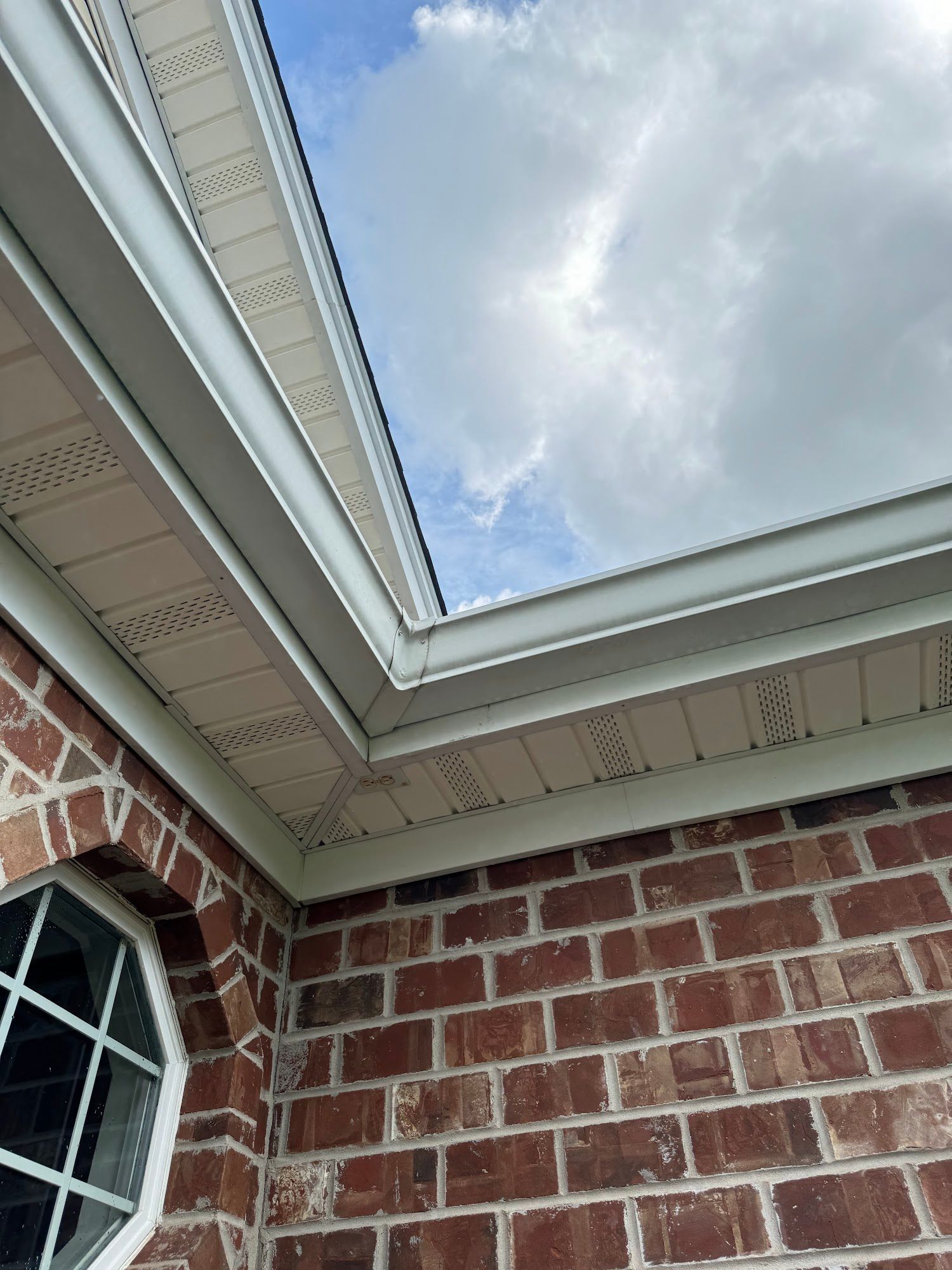 Brick building corner with white trim, angled up to a cloudy sky.