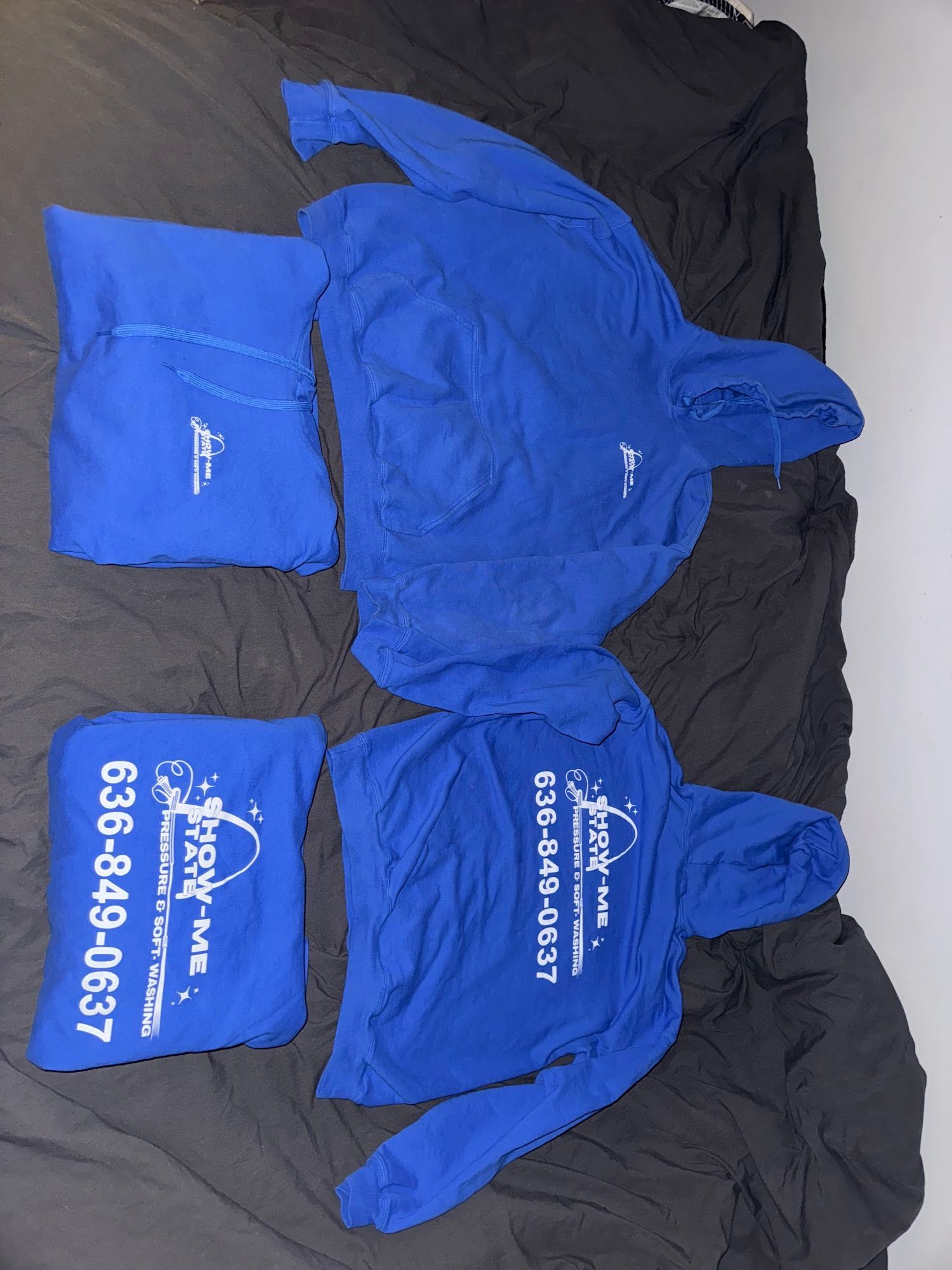 Two blue hoodies and two matching sweatpants sets on a dark gray surface, with white printed text and a phone number.