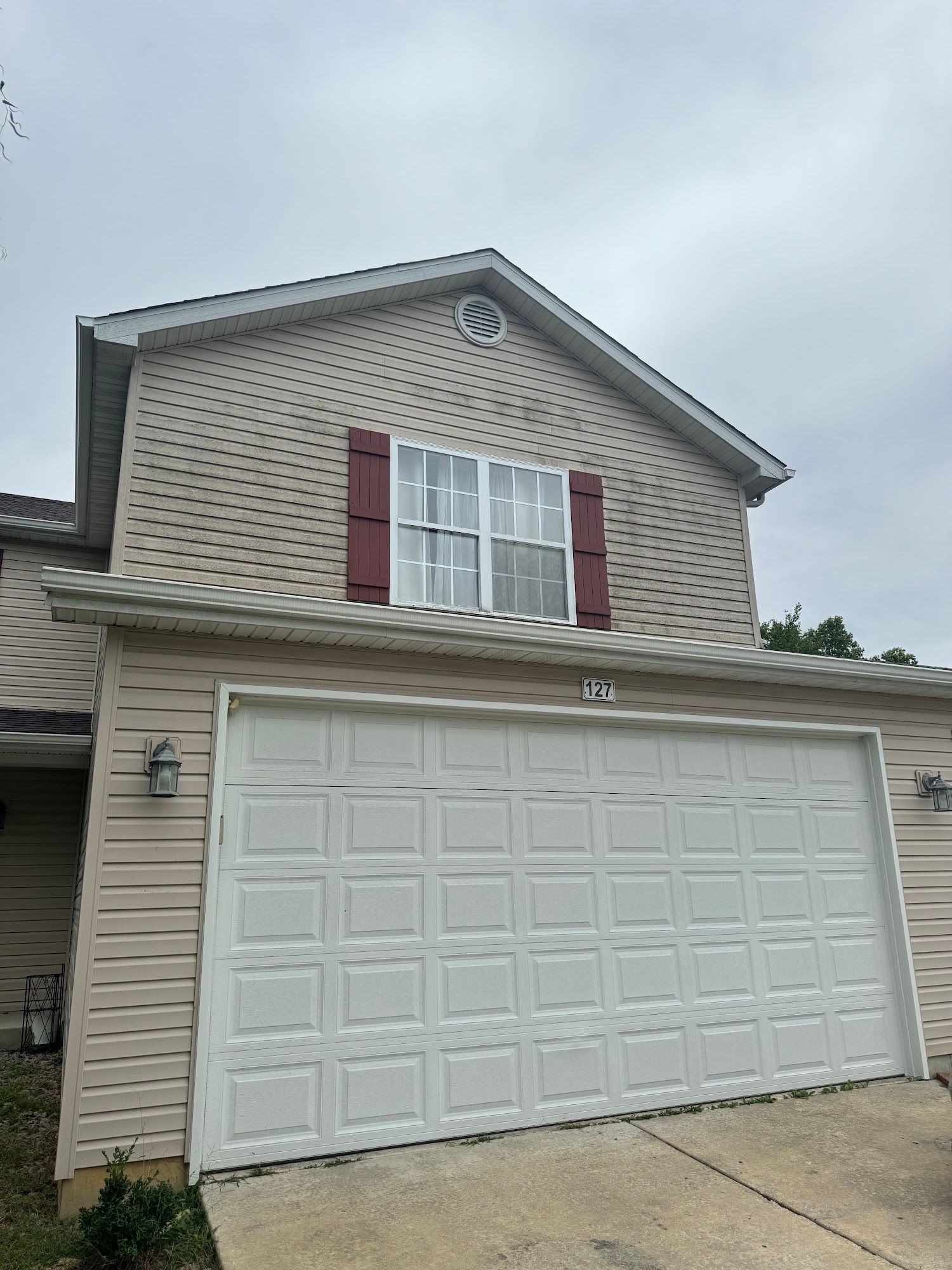 Beige house with a white garage door, red shutters, and an overcast sky.