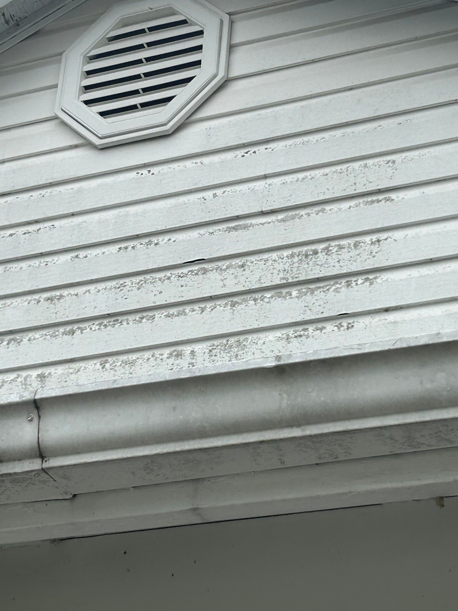 White siding with visible weathering and an octagonal vent.