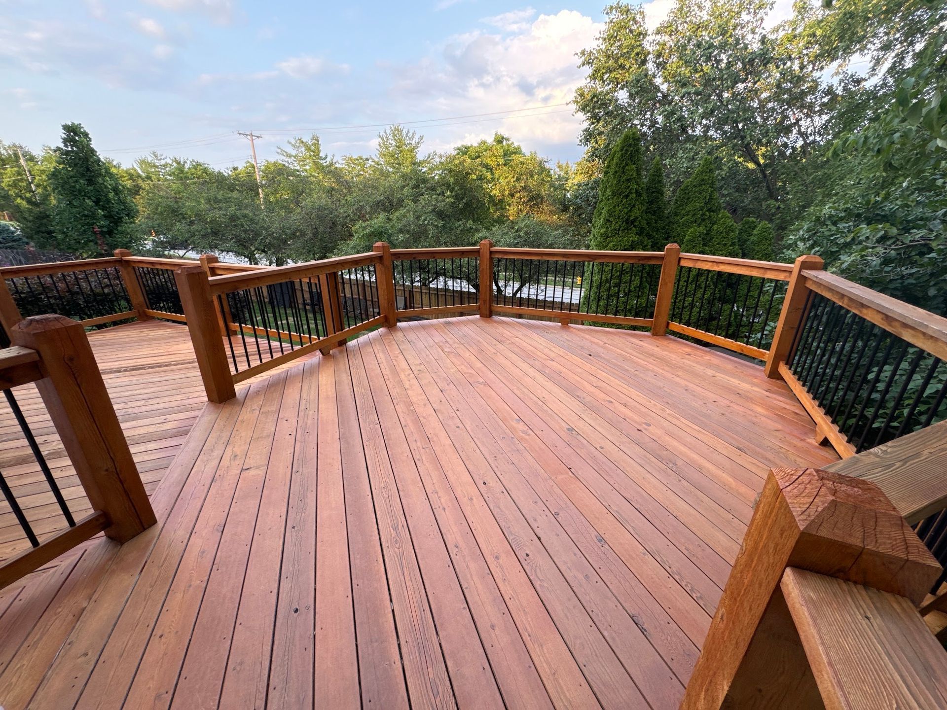 Wooden deck with railing, overlooking water and trees, on a sunny day.