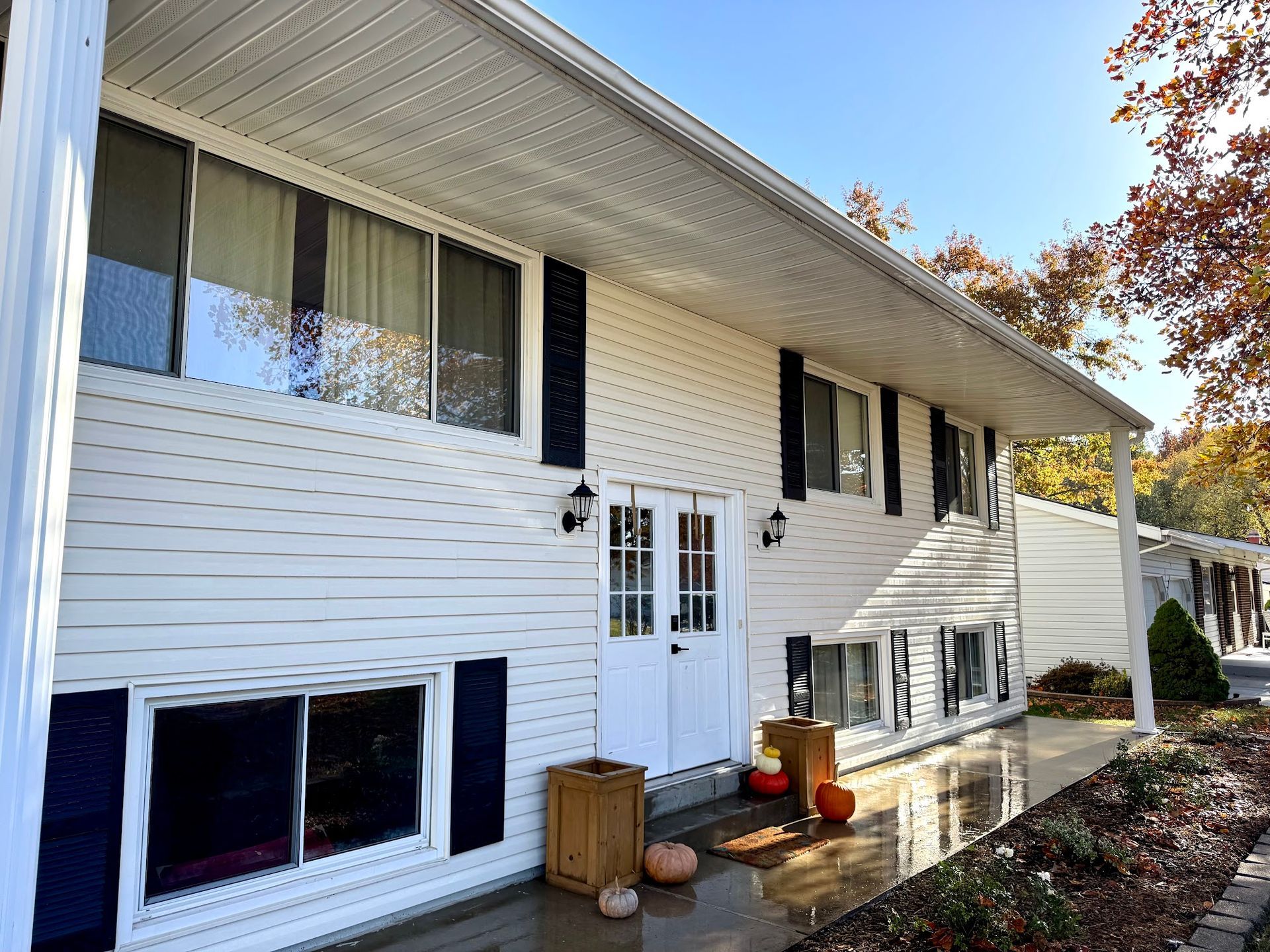 White two-story house with black shutters, double doors, and fall pumpkins on the porch.