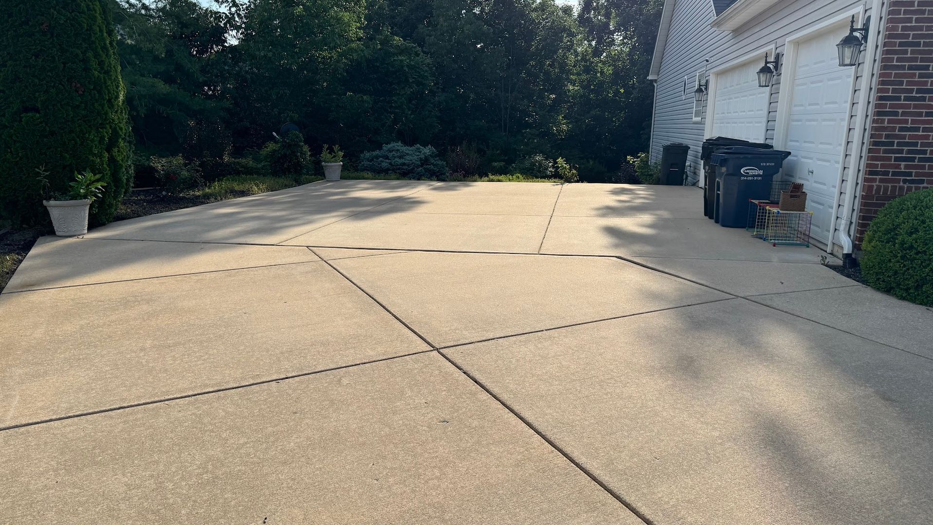 Beige concrete driveway with visible control joints, leading to a garage. Trash cans sit near the garage.