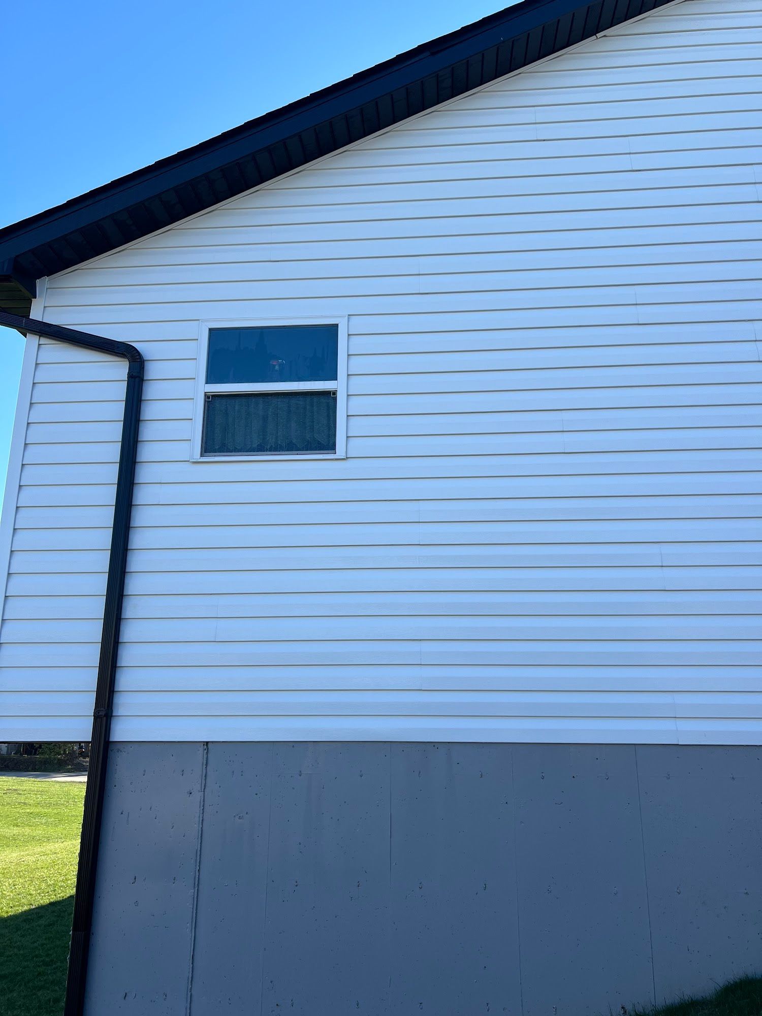 Side of a house with white siding, a window, and a dark downspout against a blue sky.