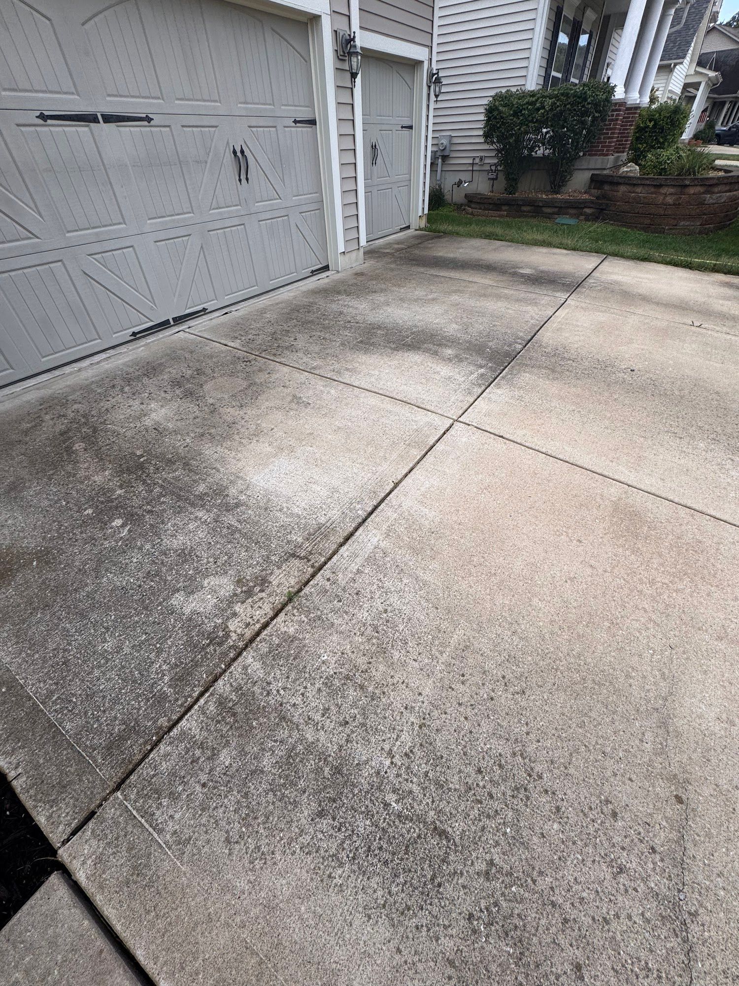 Gray concrete driveway in front of a house, stained with dirt and grime.