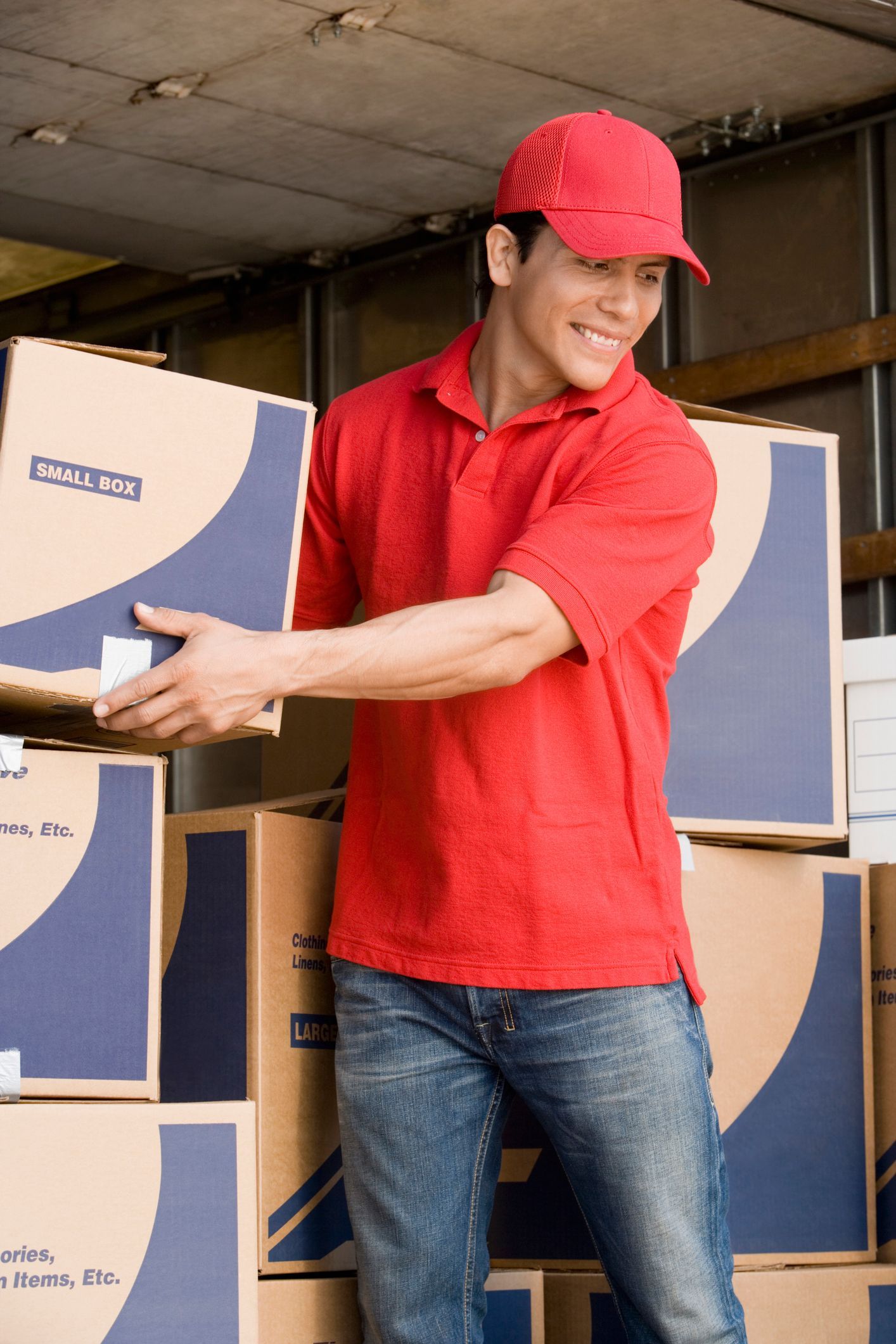 A removalist in a red uniform loading cardboard boxes into a moving truck during relocation A removalist in a red uniform loading cardboard boxes into a moving truck during relocation