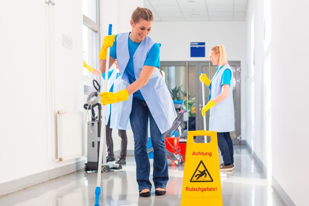 A Woman Is Mopping the Floor in A Hallway Next to A Yellow Caution Sign — Maid In Bowral in Bargo, NSW