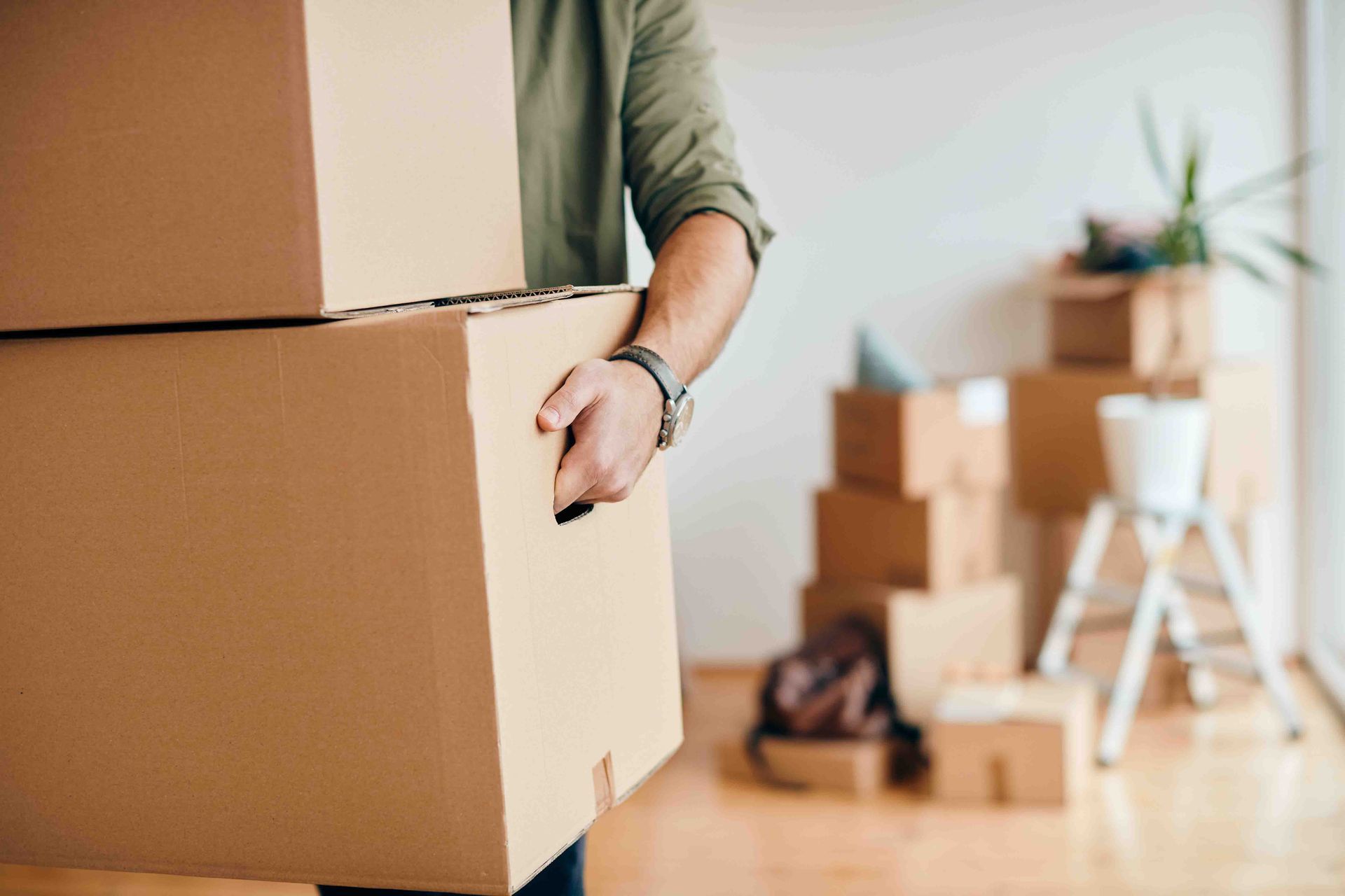 A Man Is Carrying a Stack of Cardboard Boxes in A Living Room — Maid In Bowral in Moss Vale, NSW