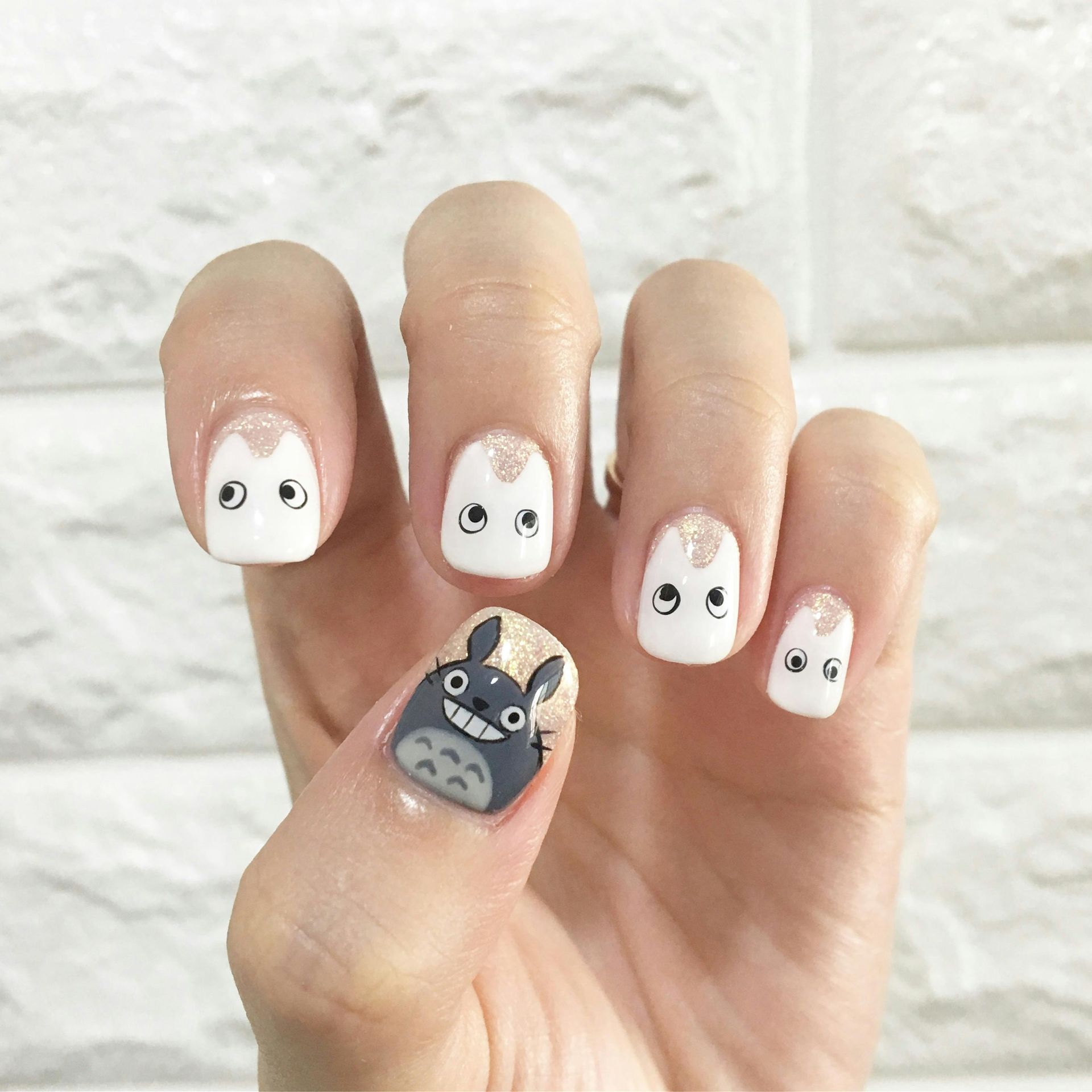 Hand with nail art featuring Totoro and white cat-like faces on a white background.