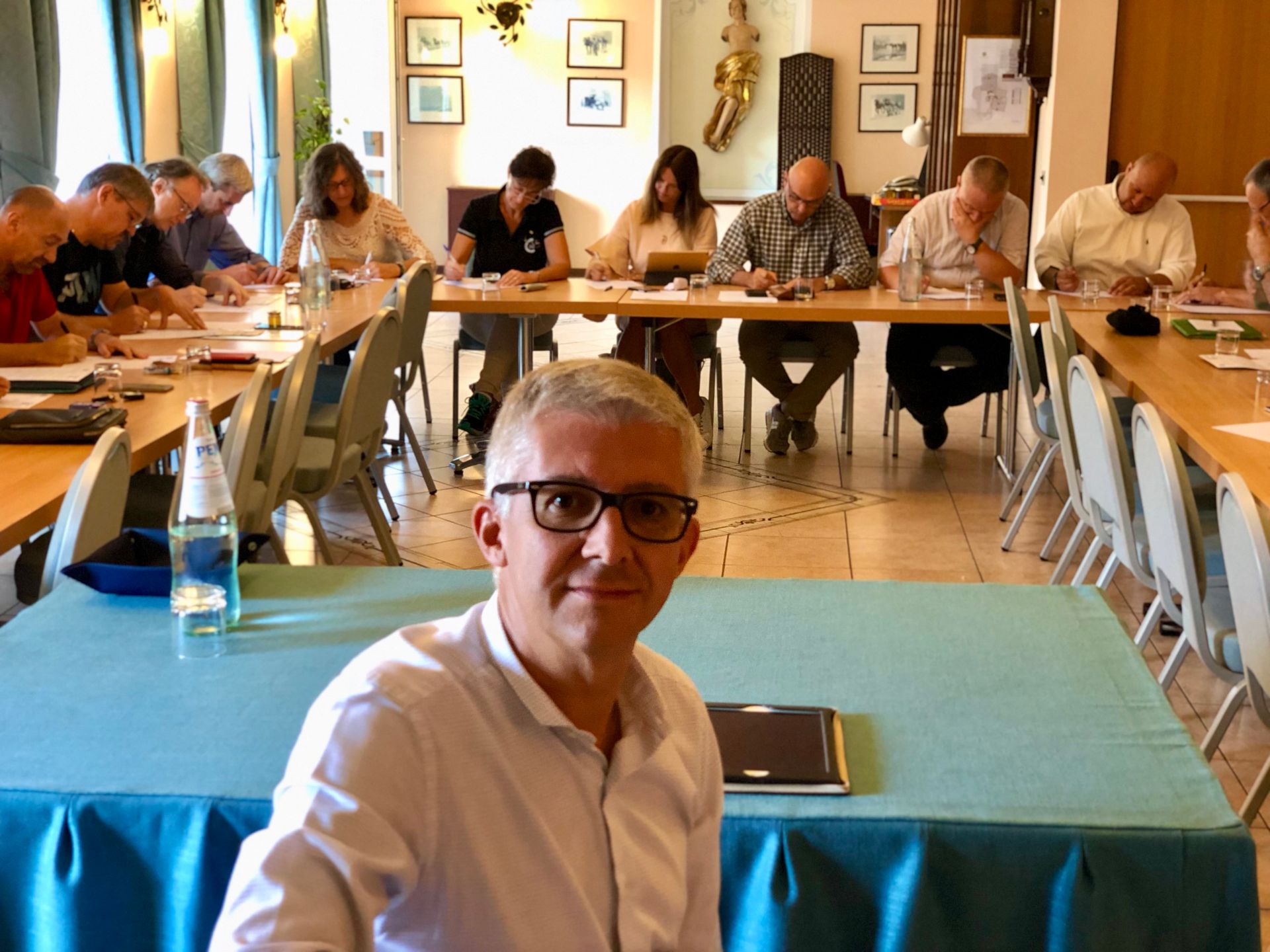 Andrea Brugnoli con gli occhiali è seduto a un tavolo davanti a un gruppo di persone sedute a tavoli