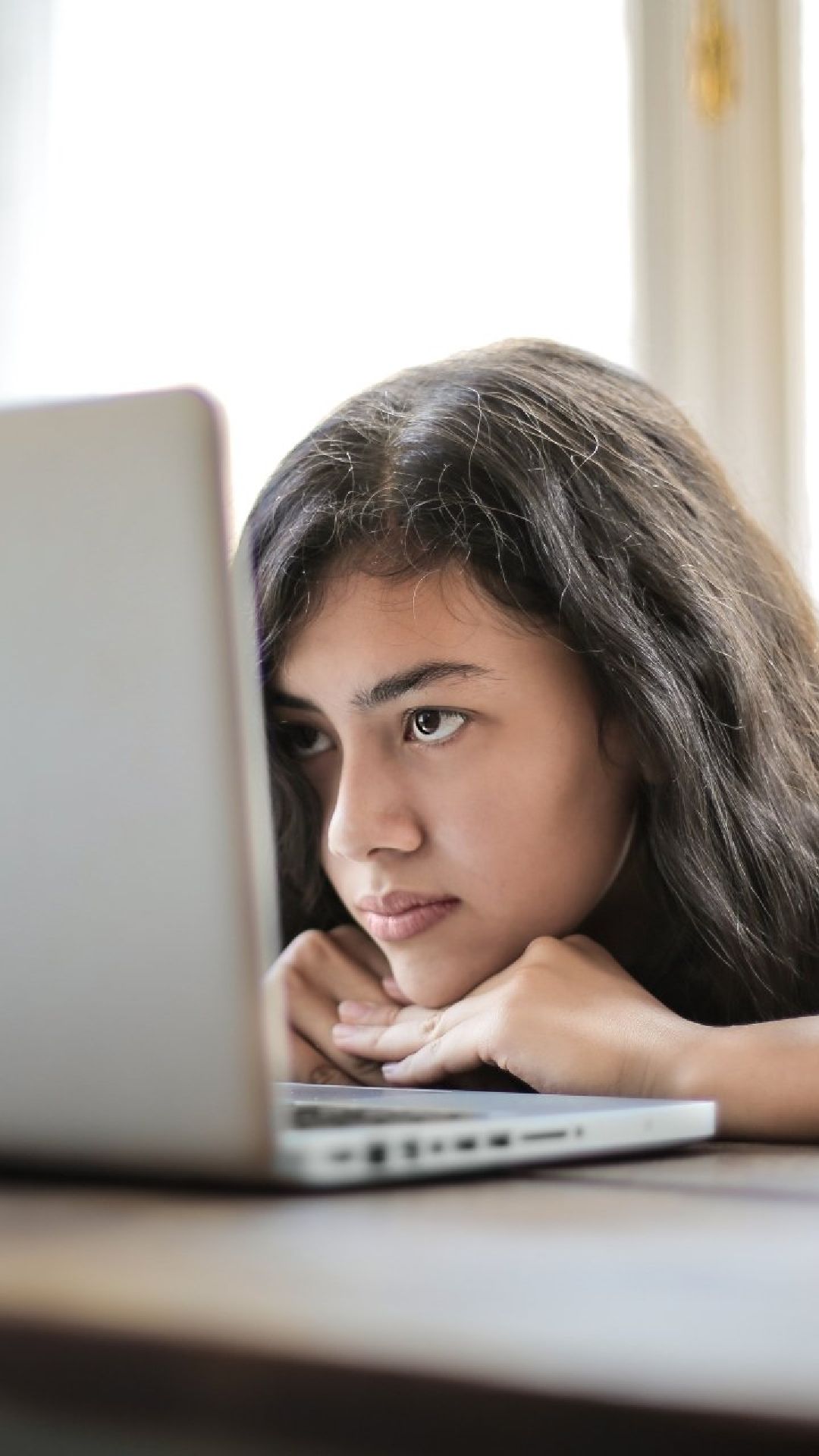 Una giovane donna è seduta a un tavolo e guarda un computer portatile.