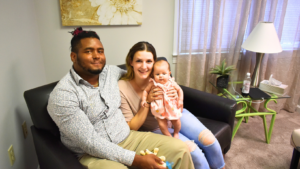 A man and woman are sitting on a couch holding a baby.