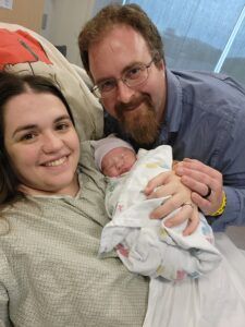 A man and a woman are holding a newborn baby in a hospital bed.