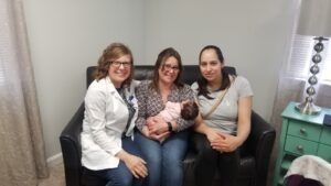 A group of women are sitting on a couch holding a baby.