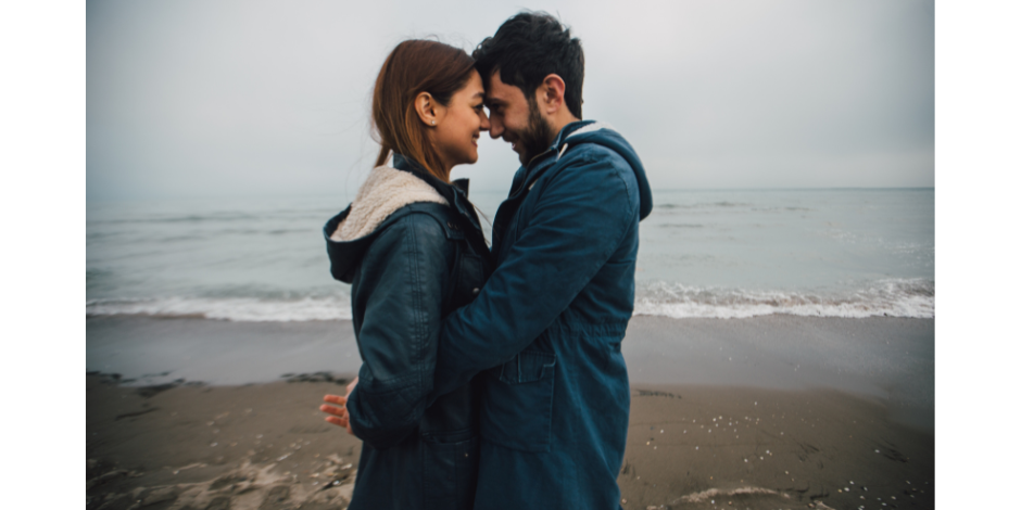 A man and a woman are touching their foreheads on the beach.