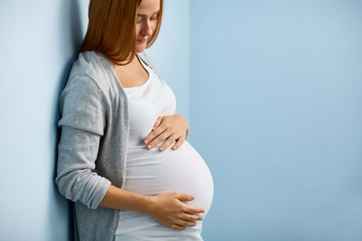 A pregnant woman is leaning against a wall and holding her belly.