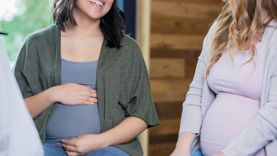 Two pregnant women are sitting next to each other and talking.