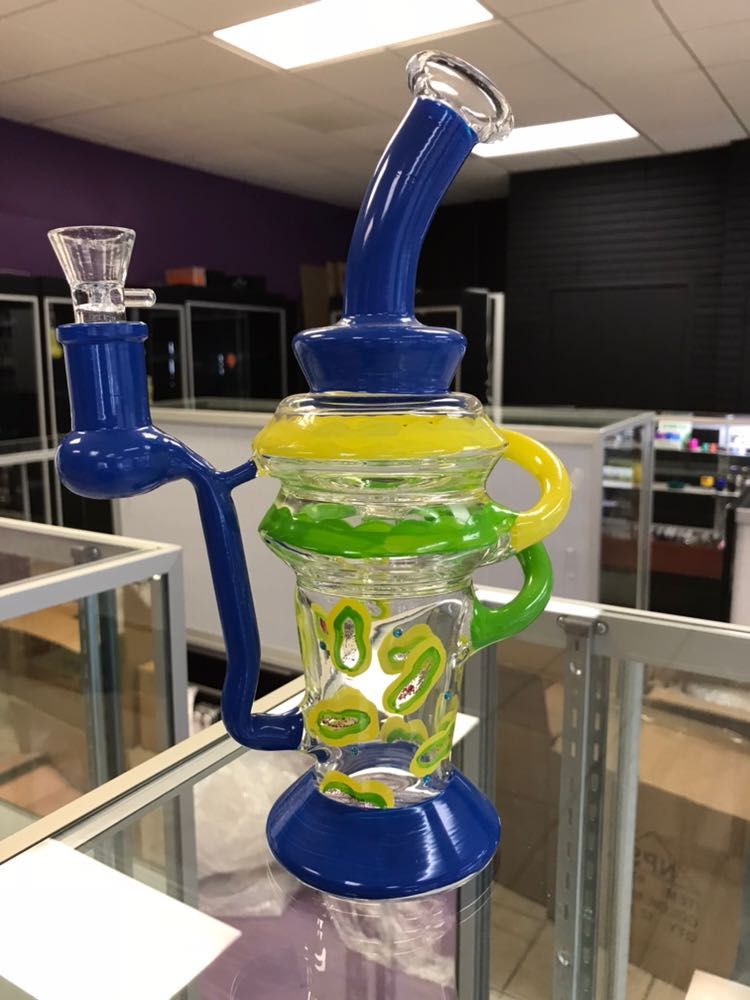 A blue and green glass pipe is sitting on a glass shelf in a store