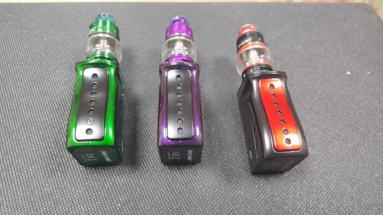 Three different colored electronic cigarettes are sitting on a black surface