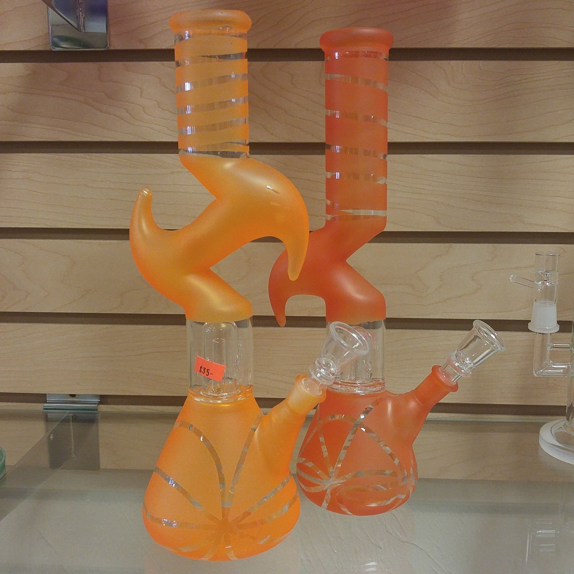 Two orange bongs are sitting on a table in front of a wooden wall