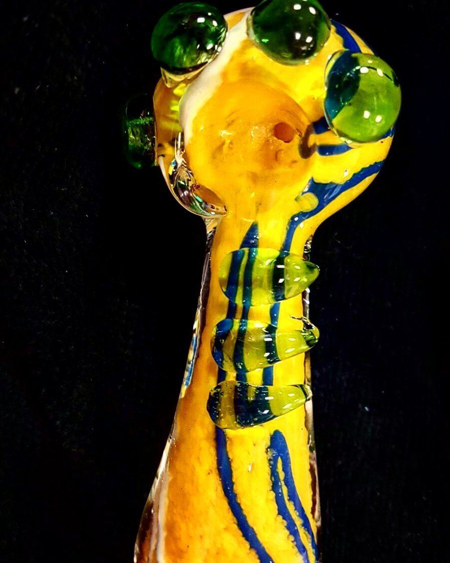 A yellow and blue glass pipe with green eyes on a black background