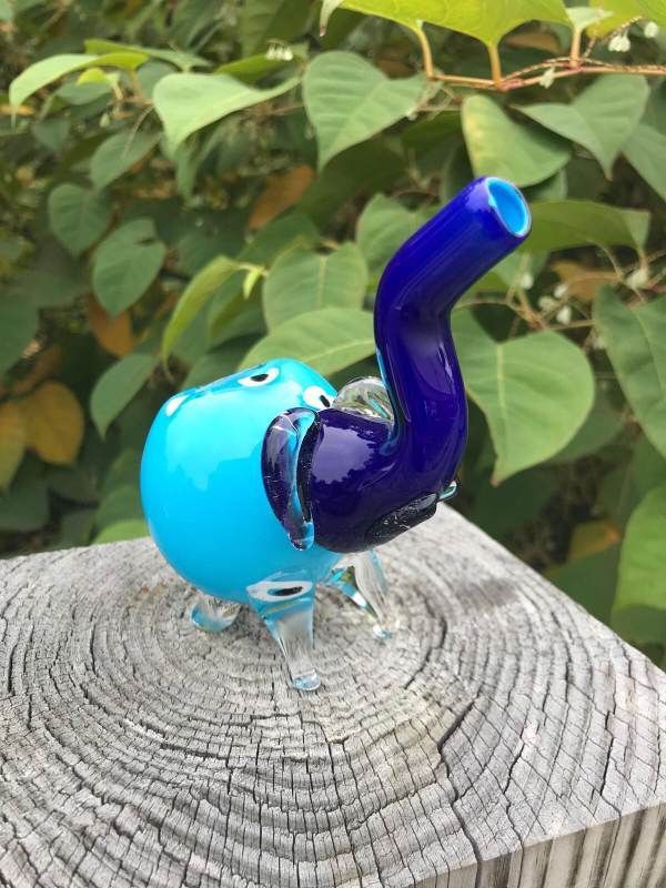 A blue and purple glass elephant pipe is sitting on top of a wooden stump