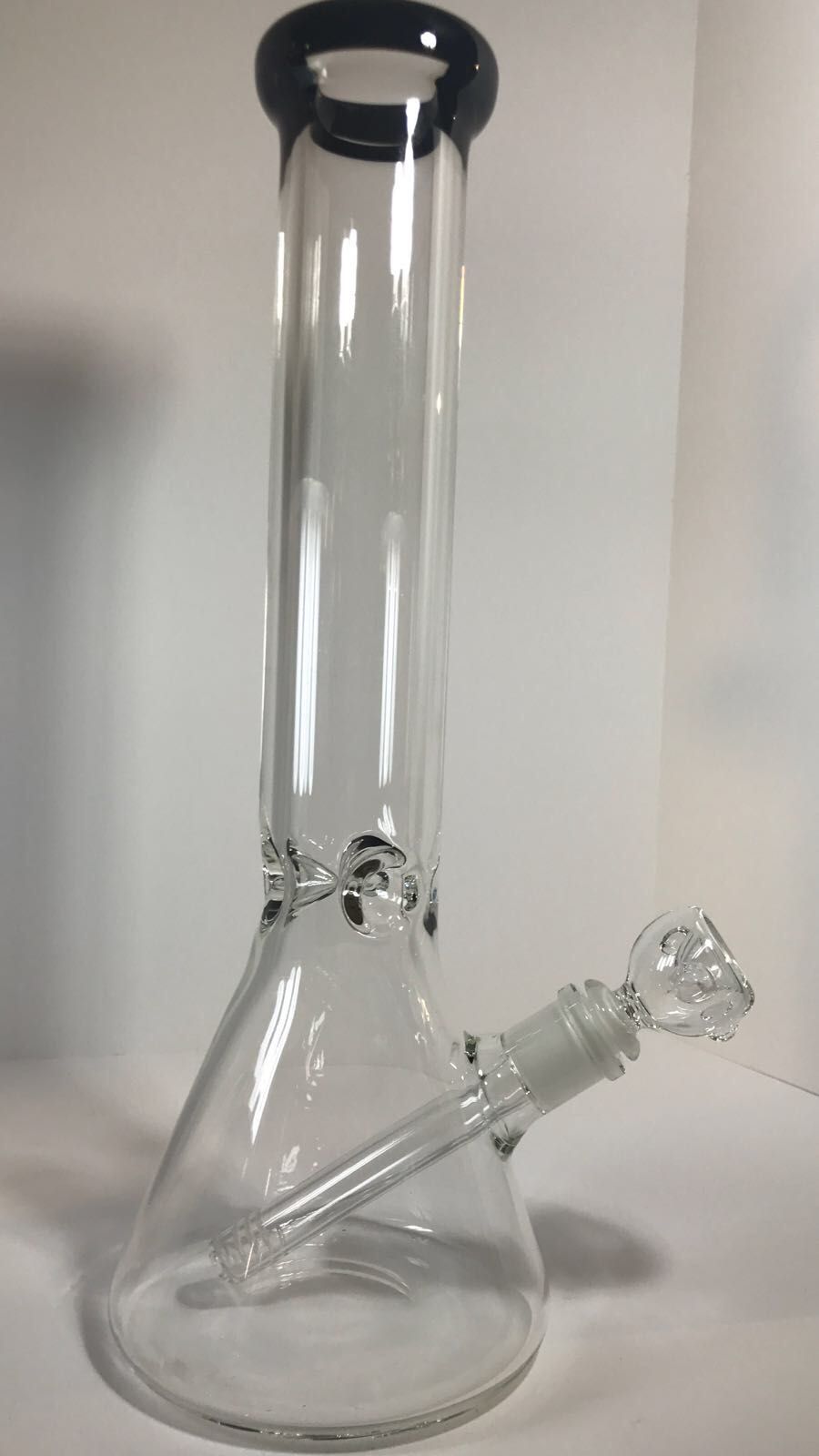 A clear glass bong with a black rim is sitting on a white surface