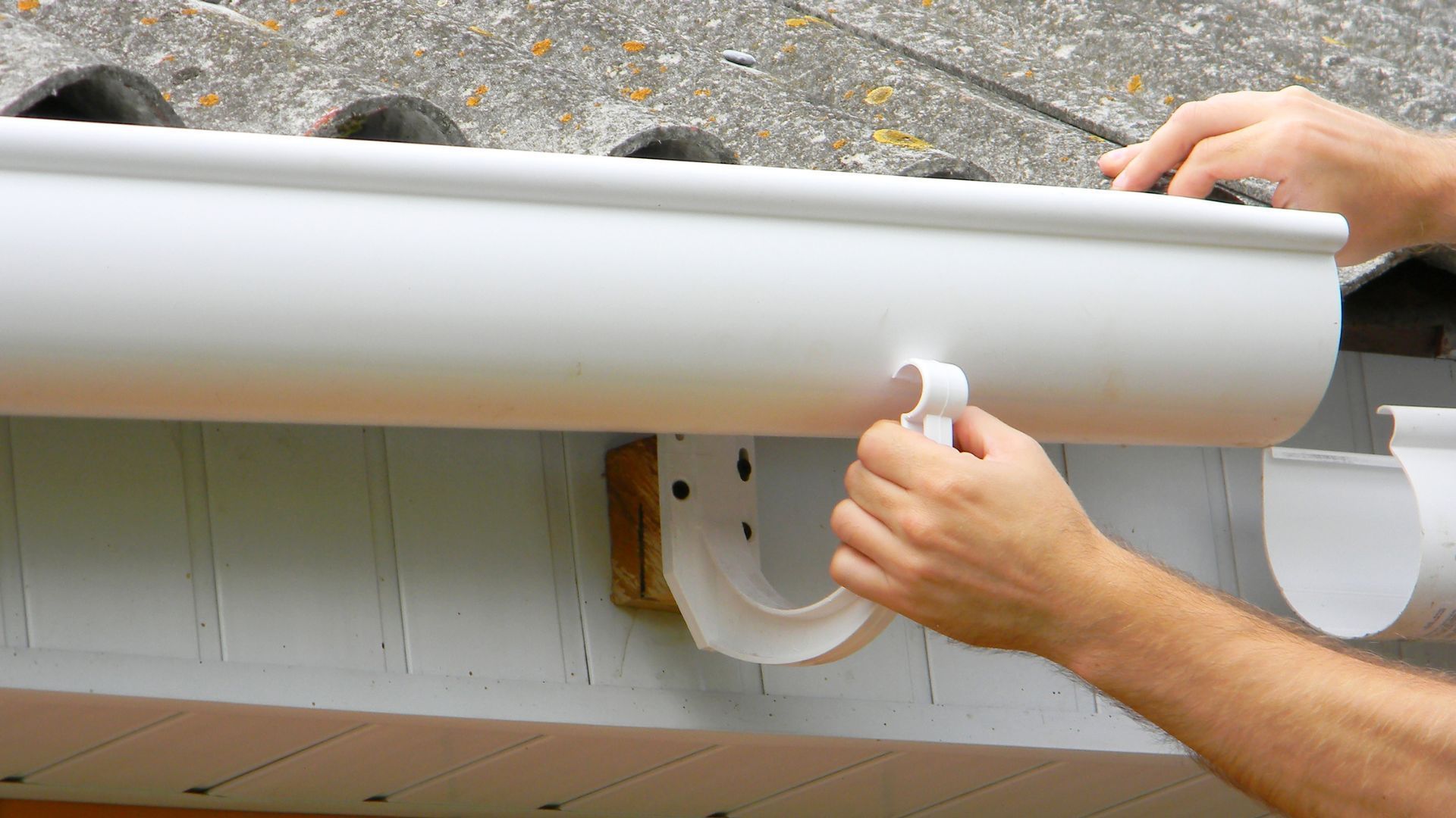 A person is fixing a gutter on the side of a house.