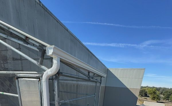 White gutter and downspout on a building with a gray facade, blue sky with contrails.