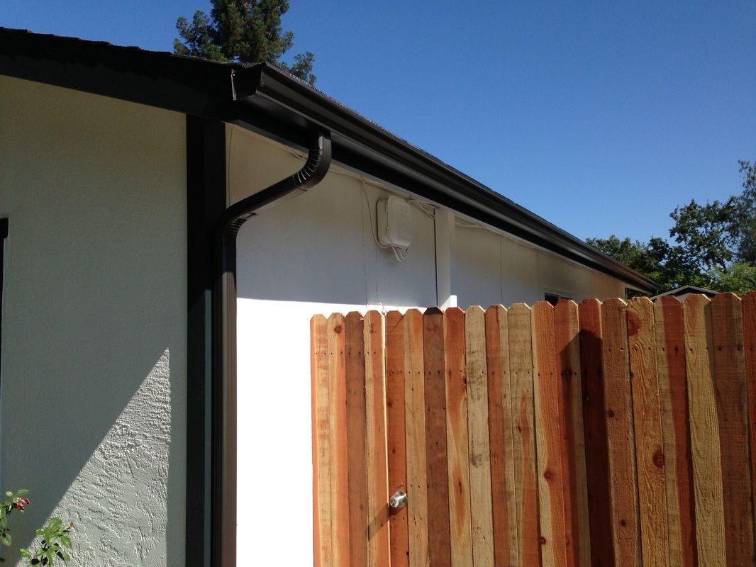 A wooden fence is next to a house with a gutter.