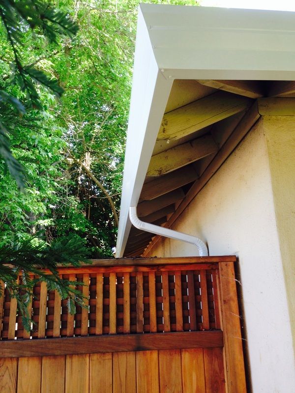 A white gutter on the side of a house next to a wooden fence
