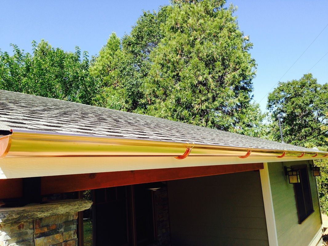 A house with a gutter on the roof and trees in the background.
