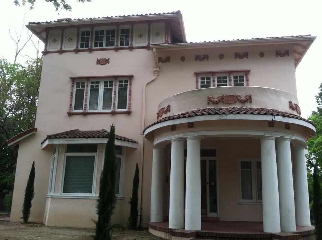 A large pink house with white pillars and trees in front of it