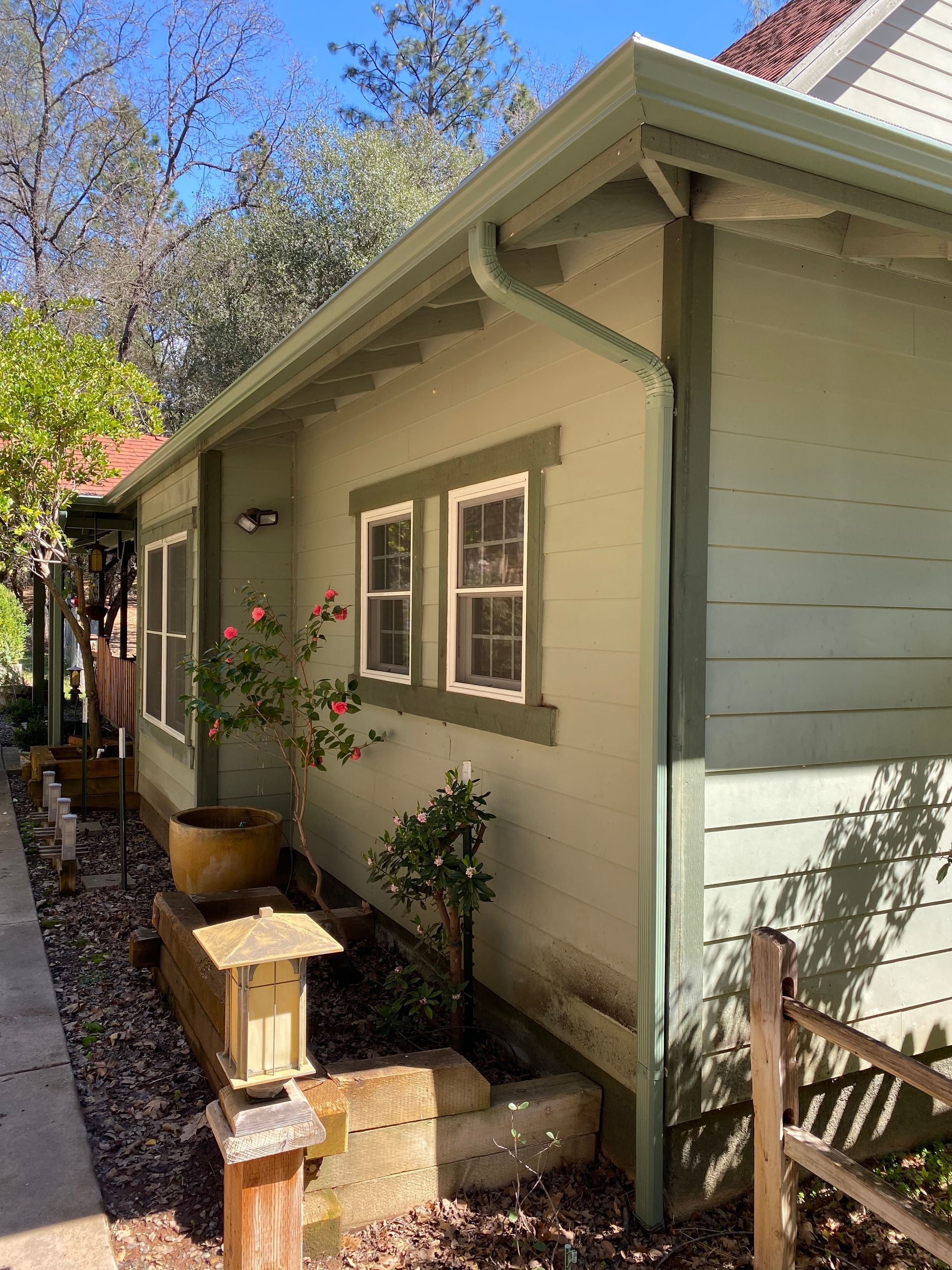 A house with a gutter on the side of it and a fence in front of it.