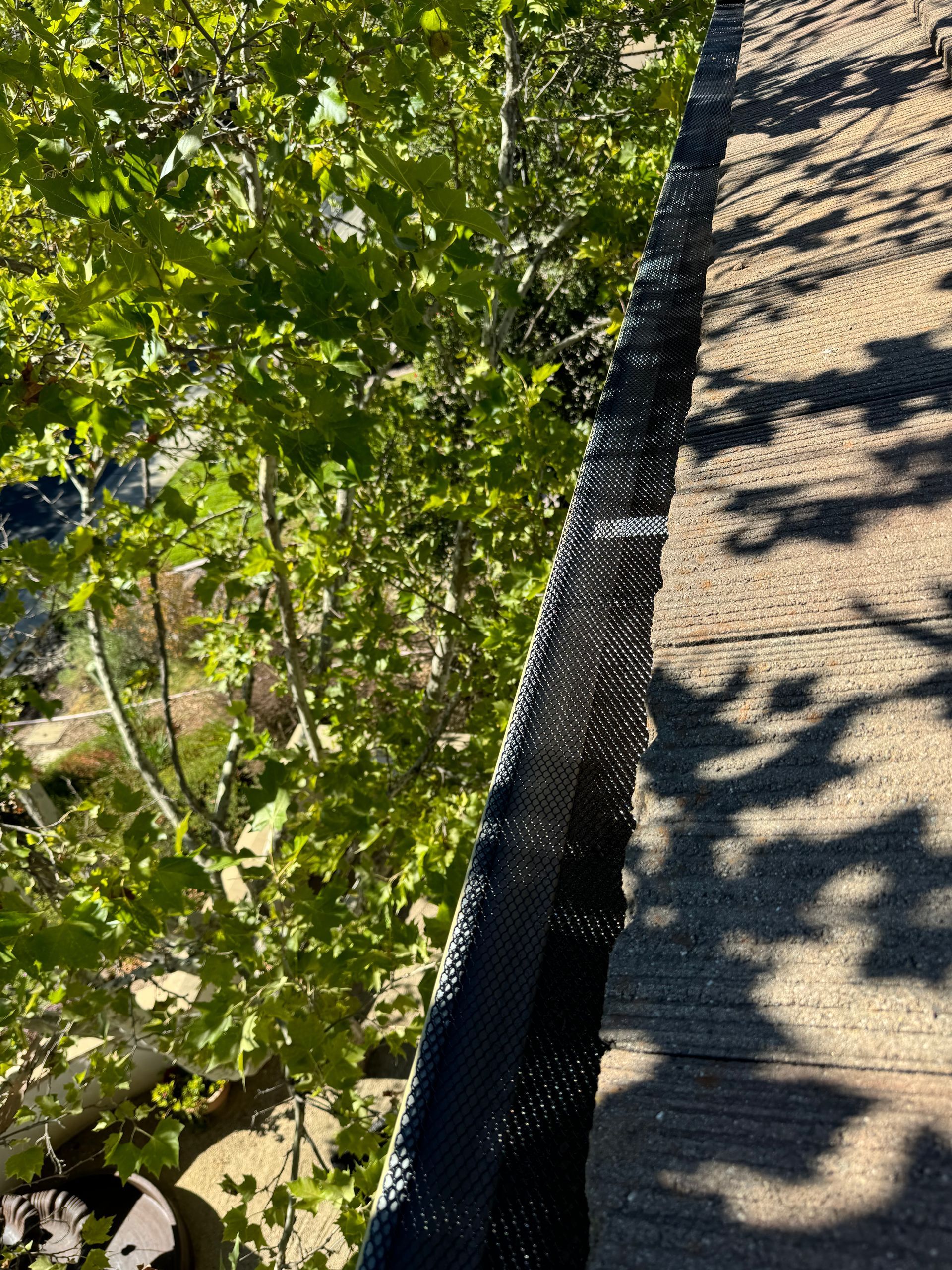 A close up of a gutter on a roof with trees in the background.