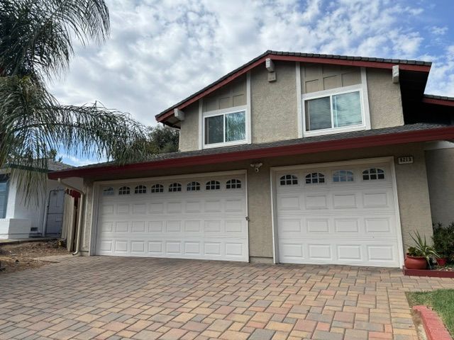 A large house with two garage doors and a brick driveway.
