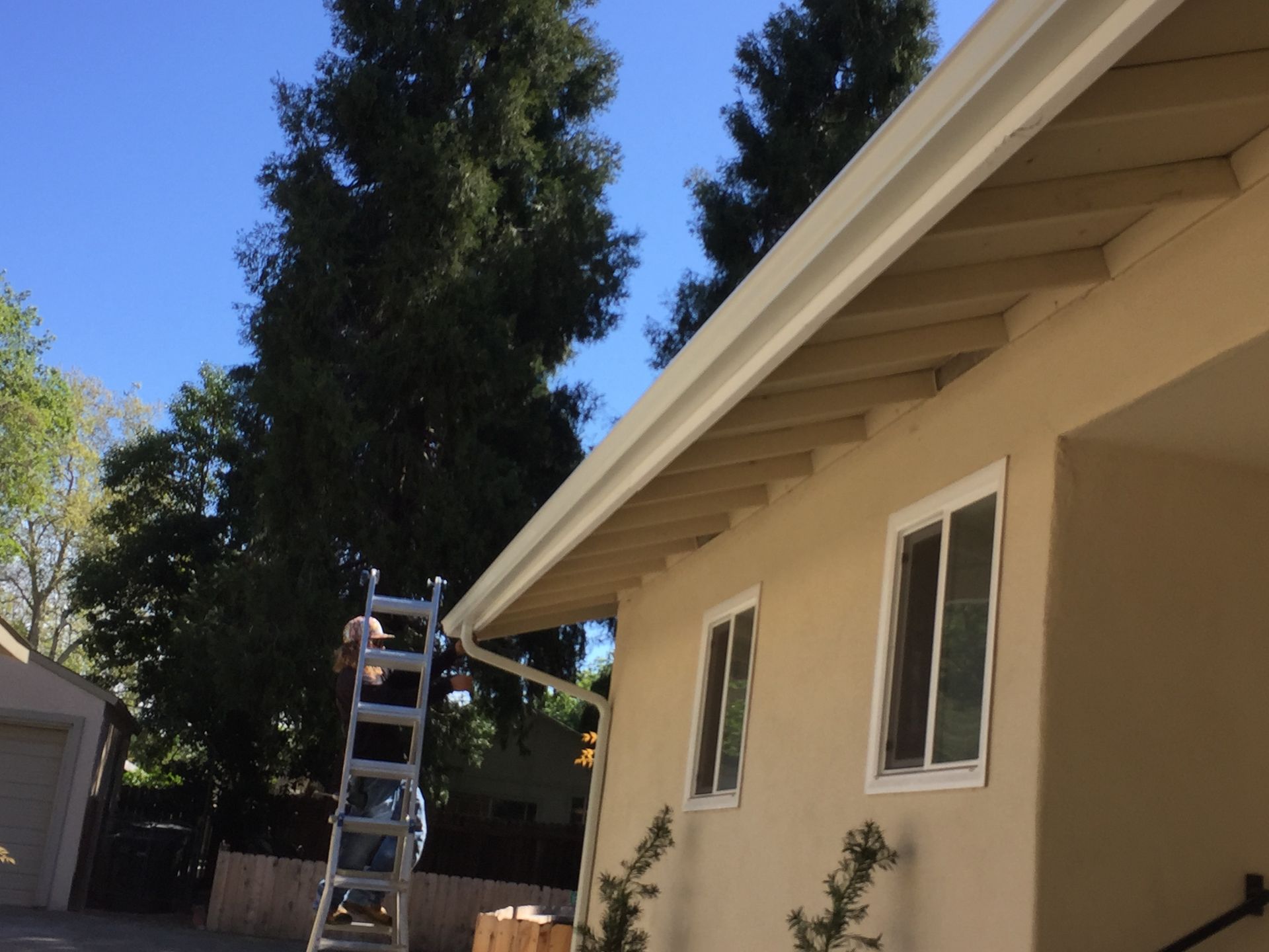 A man standing on a ladder next to a house repairing a rain gutter 