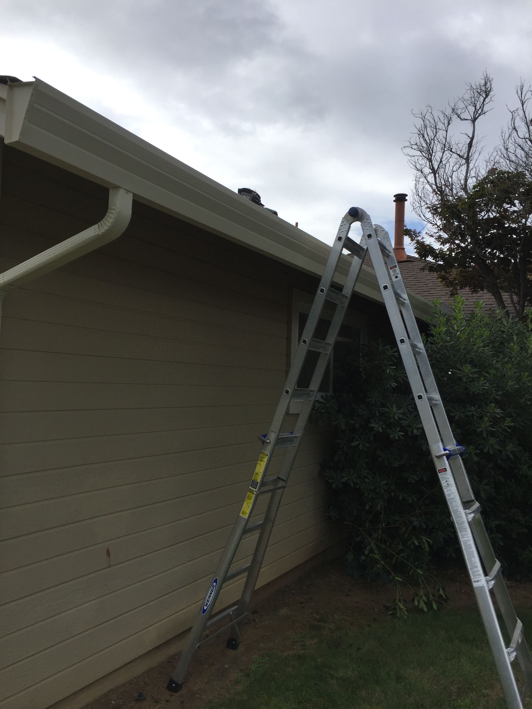 A ladder is leaning against the side of a house. Worker working on rain gutter repair
